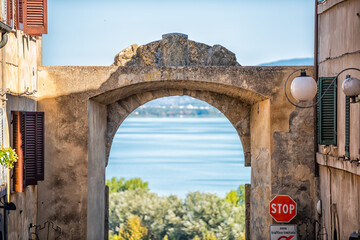 Castiglione del Lago, Italy entrance to alley street in small town village in Umbria during day on sunny summer day with arch framing lake Trasimeno blue water