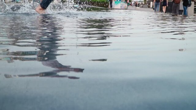 Reflection in water, jeans man does a back flip in a fountain in a city park. Close-up, slow motion