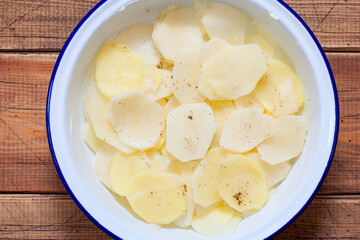 Step-by-step cooking of boulanger potato casserole, step 2 - placing the first layer of sliced potatoes in an enamel pan, top view, selective focus