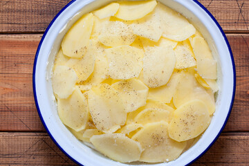 Step by step cooking boulanger potato casserole, step 4 - spreading the third layer of sliced potatoes and adding salt and pepper, top view, selective focus