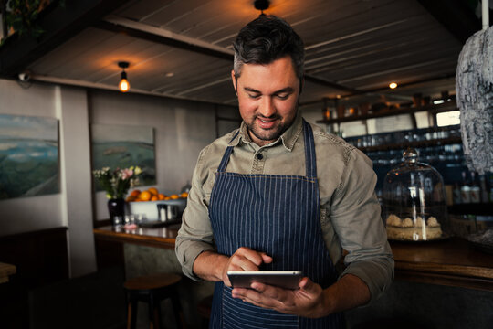 Male coffee shop owner smiling at tablet while standing in coffee shop.