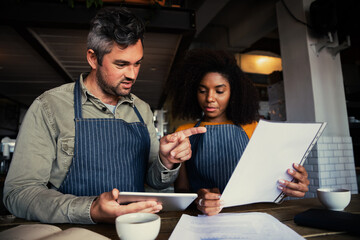 Male and ethnic female coffee shop owners discussing business in coffee shop.