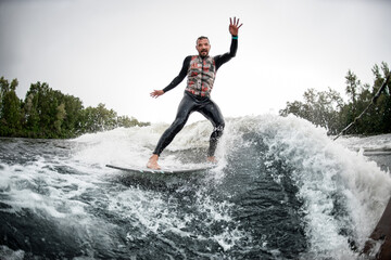 Male surfer riding foaming river wave from motorboat