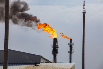 Oil refinery and gas processing plant. Orange burning gas torch with black smoke on grey sky.