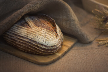 Freshly baked sourdough wheat bread laying on wooden board covered with jute.