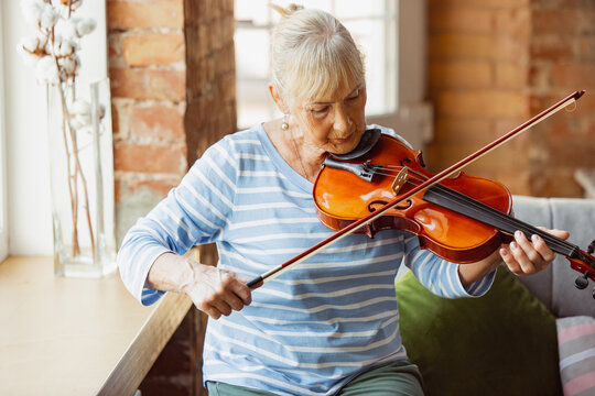 Learning to play violin online. Senior woman studying at home, getting online courses, self-development. Caucasian woman using modern devices for education, spending time for new job or hobby.