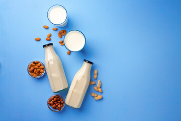 Bottles of vegan non dairy milk with various nuts on blue background