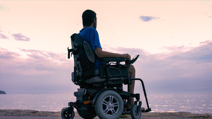 Man on wheelchair near sea at sunset.