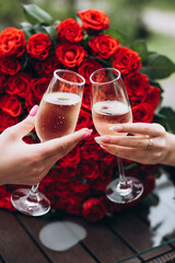 Two girls clink glasses of champagne on a bouquet of roses