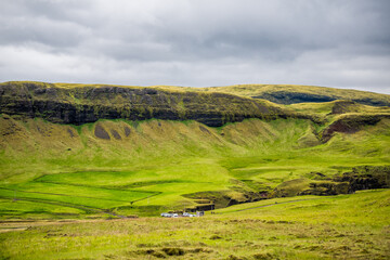 Cliff in Fjadrargljufur, Iceland with high angle view of parking lot cars by green moss grass landscape view on cloudy stormy day with clouds in sky