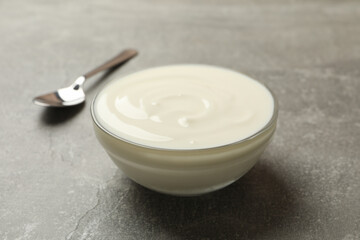 Spoon and bowl of sour cream on gray background, close up