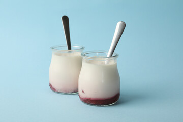Glass jars of yogurt with spoons on blue background