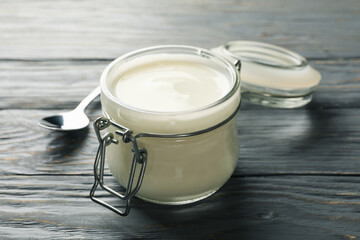Glass jar of sour cream yogurt and spoon on gray wooden background