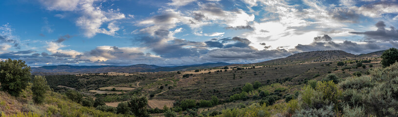 panoramic view from the mountain to the background clouds, more mountains, trees and cereal fields in the valley.