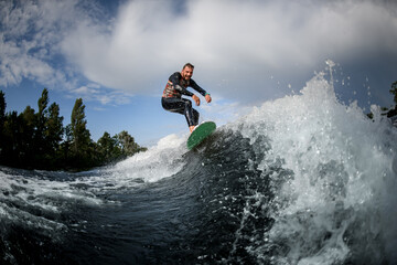 Sporty male surfer riding foaming river wave in summer sunny day