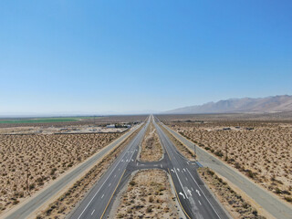 Aerial view of road in the middle of the desert under blue sky in California's Mojave desert, near Ridgecrest. Desert brush with road.