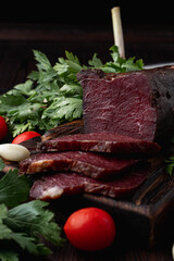 Smoked and dried mignon, juicy and yummy, on dark background with herbs and spices around, ad photo