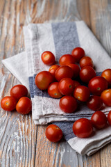 Cheap small cherry tomatoes on a wooden table and rustic linen kitchen towel, close up, beautiful advertisement photo