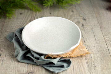 White deep plate on blue napkin and burlap. Wood background and green plants