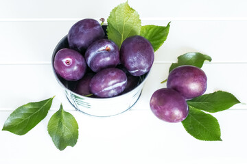 ripe plums and green leaves on a white background close-up. background with ripe fresh plums. plums in a bowl on the table.