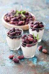 Coconut cream dessert with fresh mulberry berries in glass, selective focus
