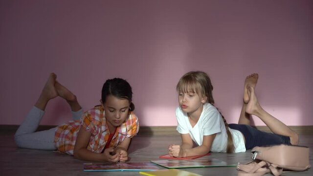 Adorable little girls study at home with books, girls playing together, drawing, doing homework at home. friends having fun learning