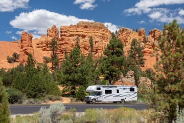 Red Canyon, UT, USA: white rv travels on a tarred road through red rock country. Pinnacles and hoodoos are visible in the background surrounded by pine trees. - obrazy, fototapety, plakaty