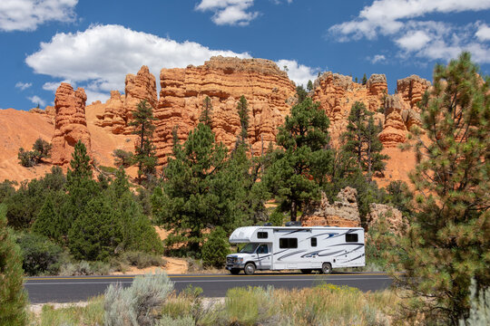 Red Canyon, UT, USA: white rv travels on a tarred road through red rock country. Pinnacles and hoodoos are visible in the background surrounded by pine trees.