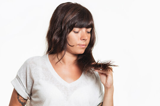Portrait of a woman with a tattoo on her arm examines the tips of her hair. Copy space. White background. Hair care concept