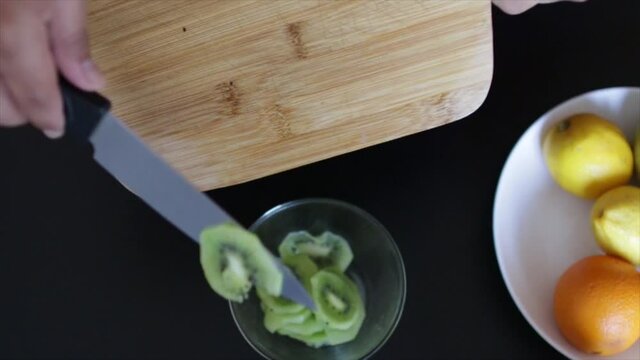 Manos picando kiwi en una tabla 