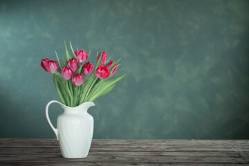 beautiful tulips in white jug on dark background