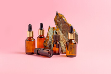 An amber bottle for essential oils and cosmetics stands next to the stone. Glass bottle on a pink...