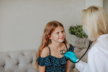 Doctor inspecting by stethoscope a girl in the grey room. Focus is at the girl.