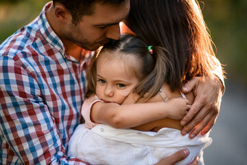 close-up of mother and father who hug their little daughter with ponytails