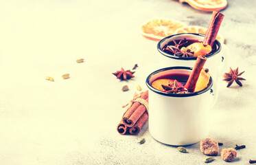 Mulled wine in white metal mugs with cinnamon, spices and orange on gray background, traditional drink on winter holiday. Copy space