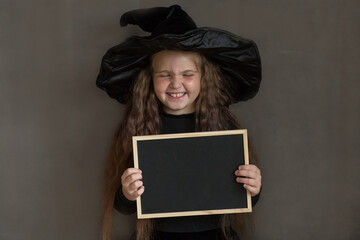 Wow girl in halloween witch costume with black desk on gray background 