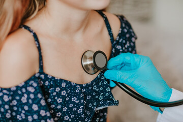 Doctor inspecting by stethoscope a girl in the grey room.