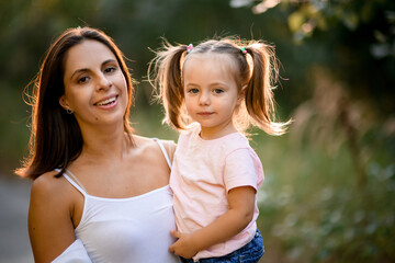 portrait of beautiful woman who holds in her arms little lovely girl with ponytails