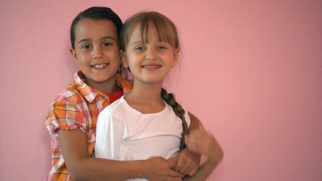 little smiling girls, sisters, best friends hug on a pink background, children hug each other