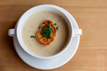 Cream soup with croutons in a white plate on a wooden table. Top view. Close-up. Space for text.