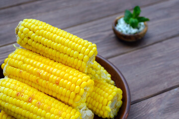 Young sweet tasty grilled corn with spicy lime oil in a clay plate on a wooden dark background. Summer food.