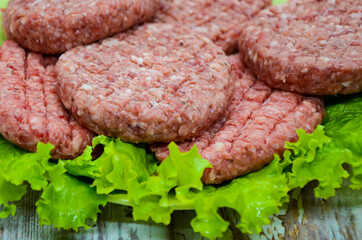 Close-up raw homemade chopped beef burgers on a plate and green salad on wooden table. BBQ preparation, beef products, traditional meat dish. Balanced diet. 