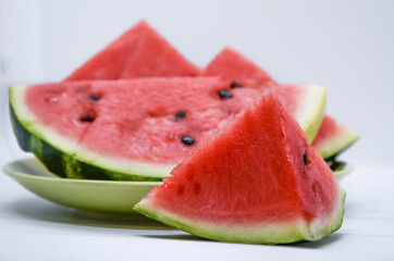 Close-up of triangular piece of watermelon and a plate of watermelon slices on white background....