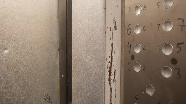 The metal elevator doors close automatically. Badly worn interior of an elevator car in a residential building. Vandal-proof armored metal panel with numeric keypad. Moving mechanical door