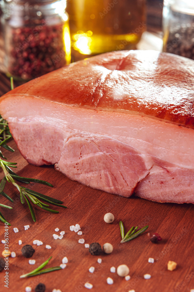 Wall mural piece of bacon with rosemary branch and spices on the wood background - close-up