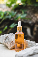 Bottles of orange serum next to natural stones against a gray wall with grape leaves with natural light. Trendy style. Grape extract. Cosmetic mockup. Copyspace.