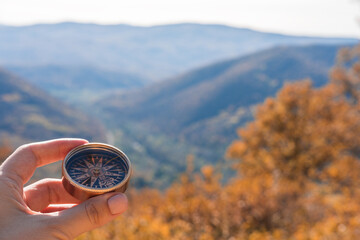 Female hand of traveler, hiker with compass on background autumn forest landscape with mountains on the horizon in orange colors in fall.
