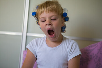 Little girl in the morning with curlers yawns