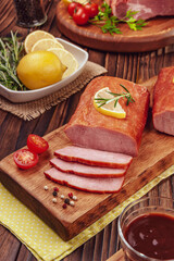Piece of smoked pork loin with rosemary branch, lemon, bbq sause and spices on the wood background