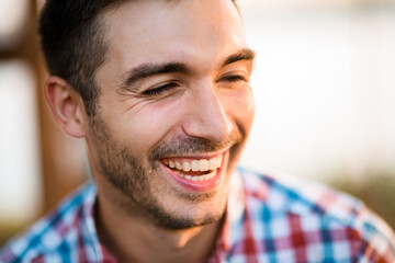 Fototapeta premium portrait of young laughing man with dark hair in shirt on blurred background.